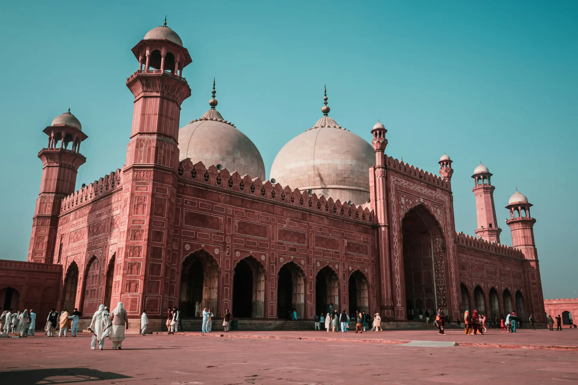 The Badshahi Mosque in Lahore, its red sandstone walls and white marble domes under a clear sky.
