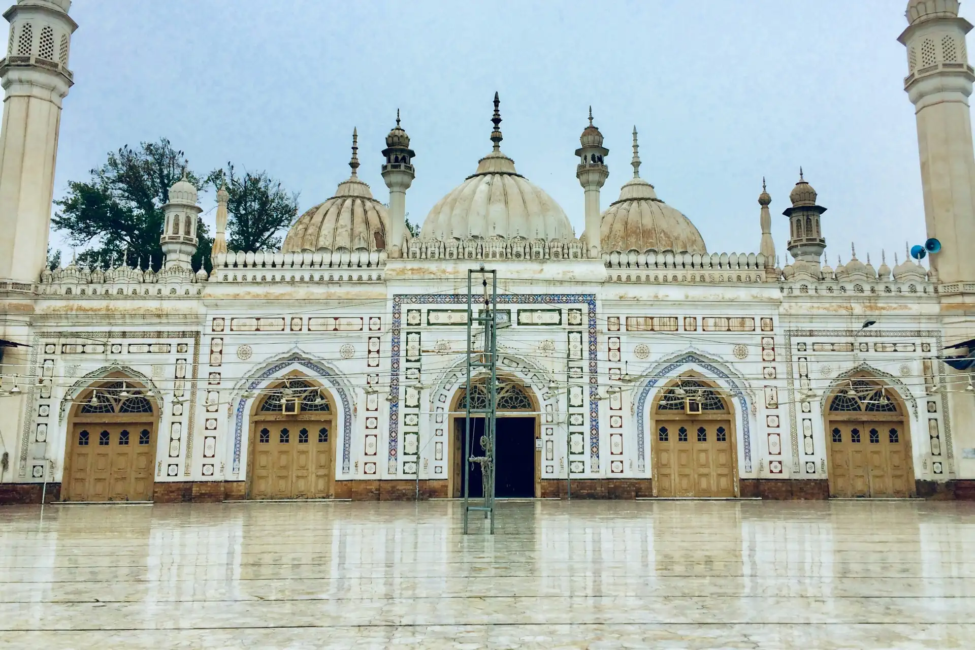 A white mosque with three domes and tall minarets in Peshawar.